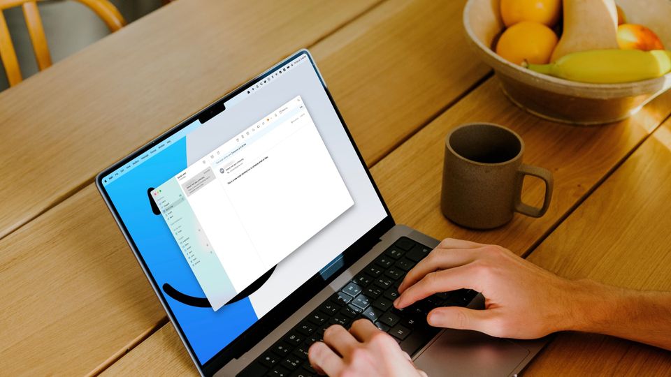 MacBook pro on wooden table with a cup and bowl of fruit next to it. Hands scheduling an email using the default mac app