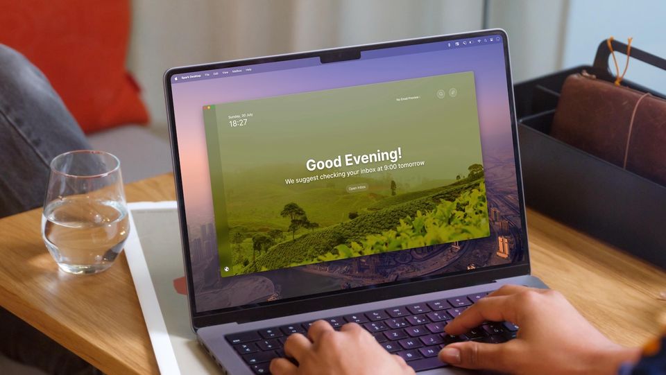 Man using Mail app on MacBook Pro on wooden table with a glass half filled with water beside it